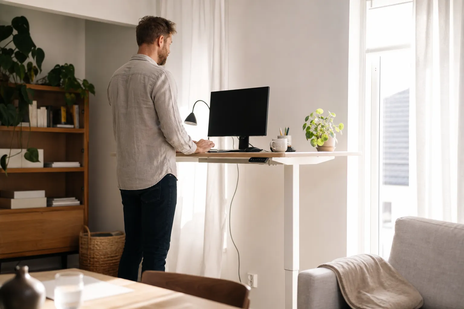 Person som arbetar stående vid ett höj- och sänkbart skrivbord i ett ljust hemmakontor